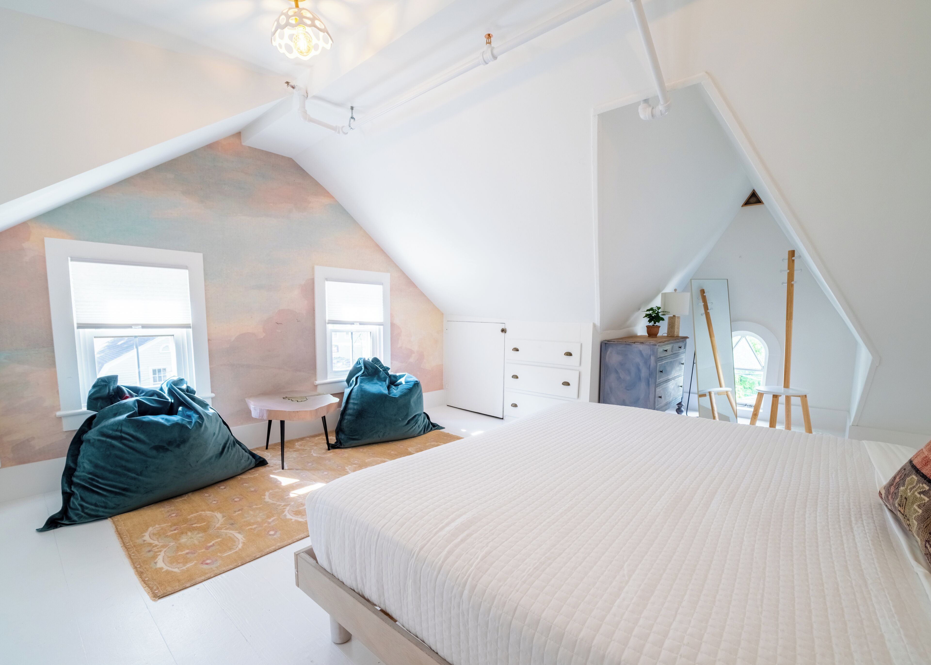 A bedroom with a sloped ceiling, a bed, a desk, and a chair.
