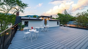 Een houten terras met zitplaatsen buiten en een huis op de achtergrond.