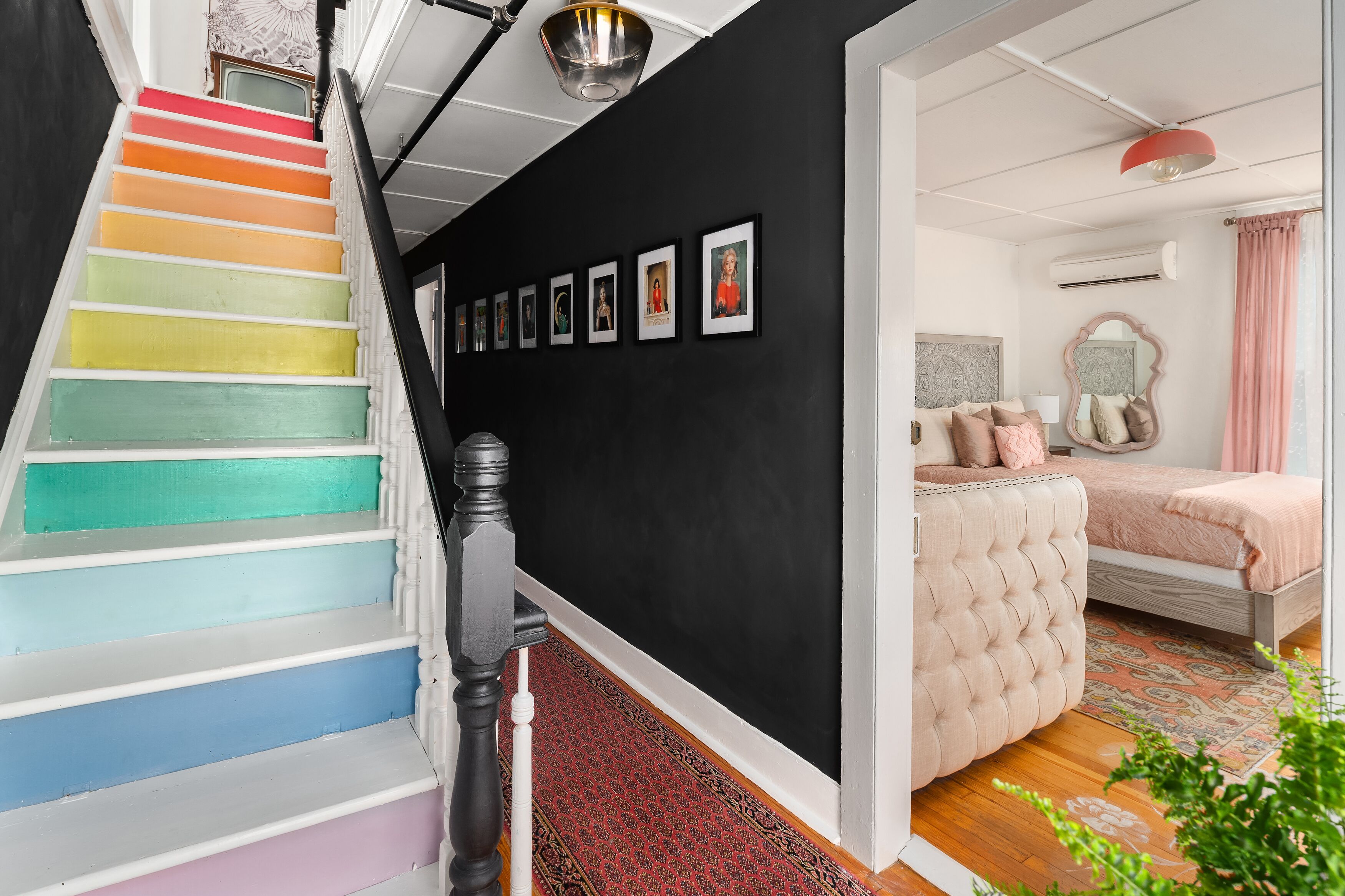 A staircase with colorful steps leading to a bedroom with a bed, a mirror, and a red lamp.