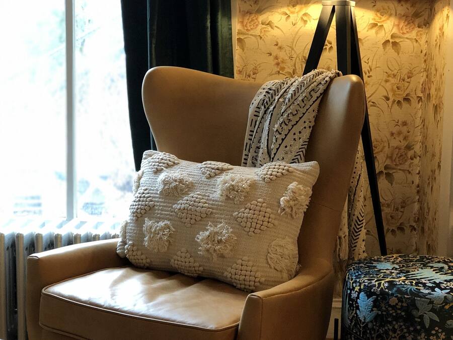 A cozy room with a leather armchair, a patterned throw pillow, a small table, and a lamp.