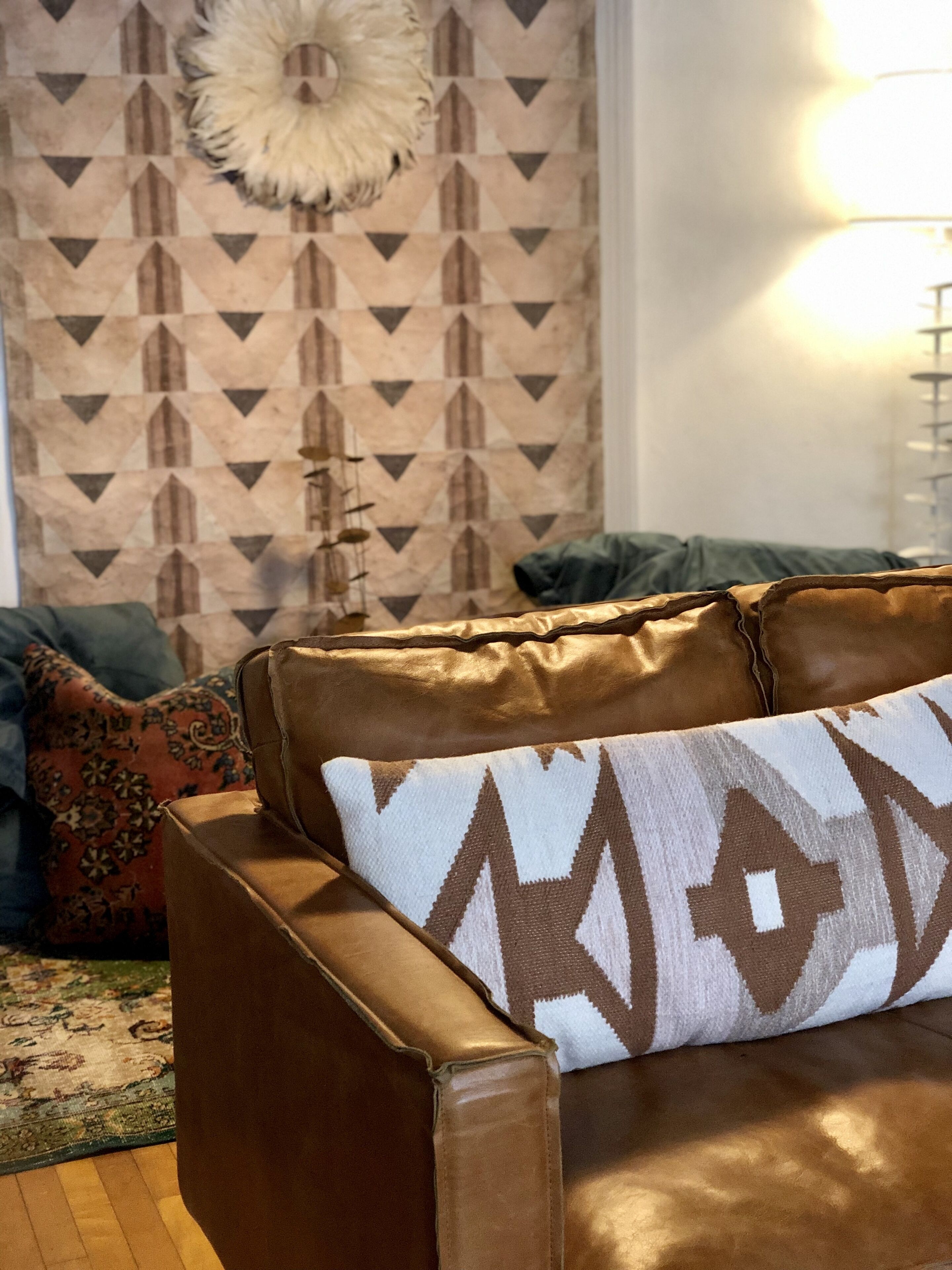 Ein braunes Ledersofa mit einem gemusterten Kissen, einer Wanddekoration und einer Lampe.