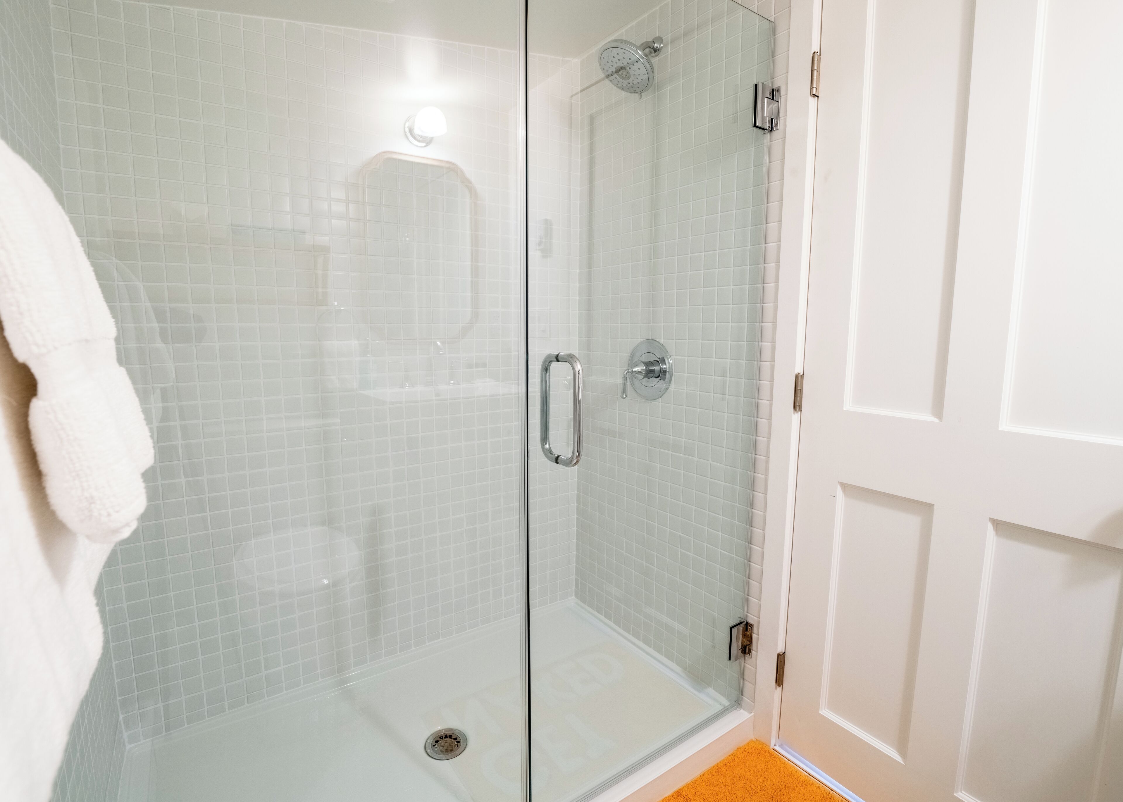 A glass-enclosed shower with a white tiled wall and a white door.