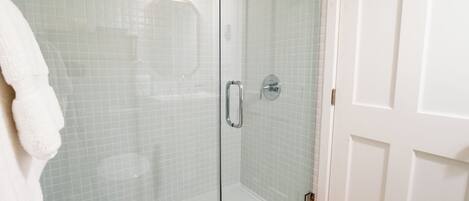A glass-enclosed shower with a white tiled wall and a white door.