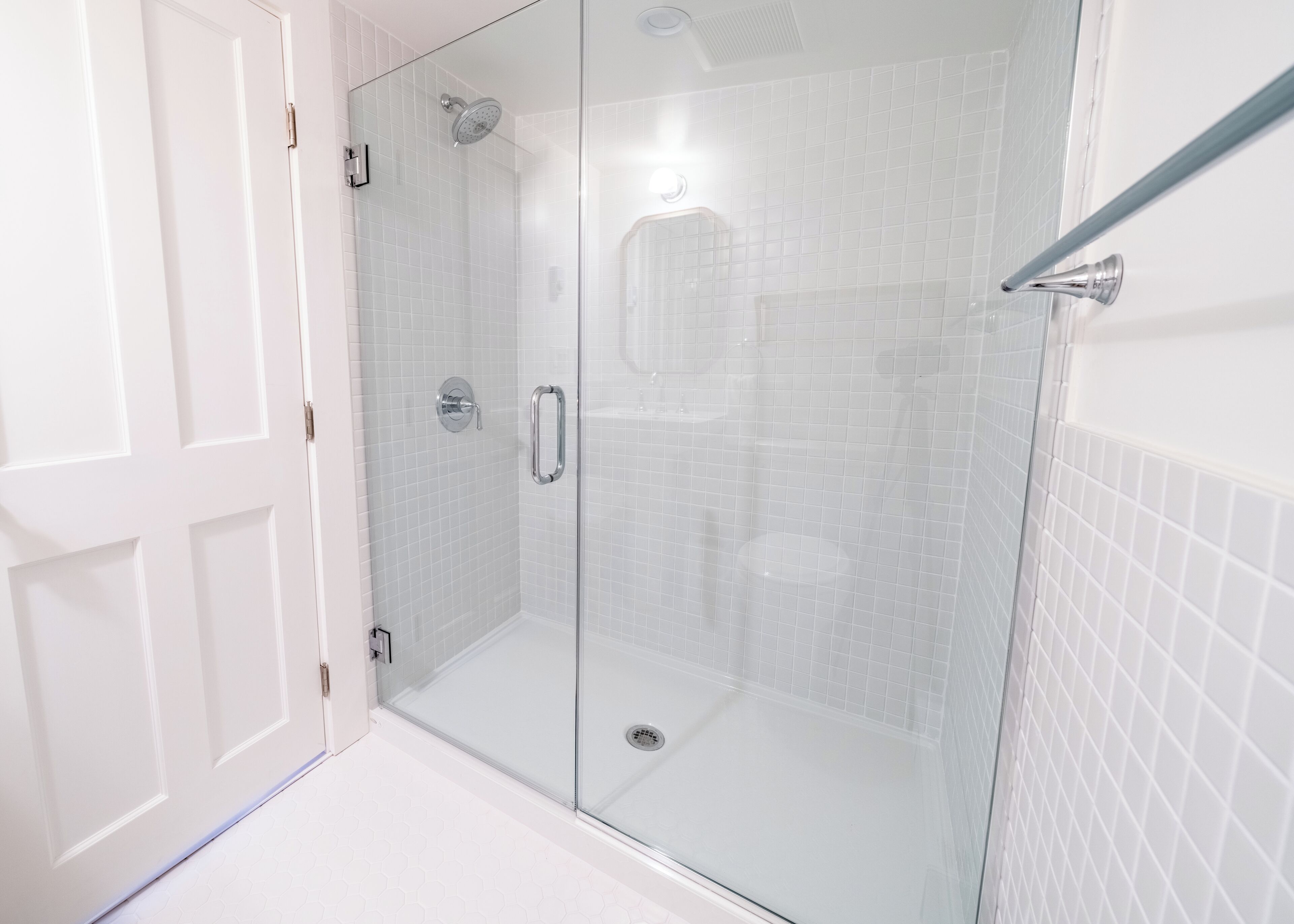 A glass-enclosed shower with a white tiled wall and a door.