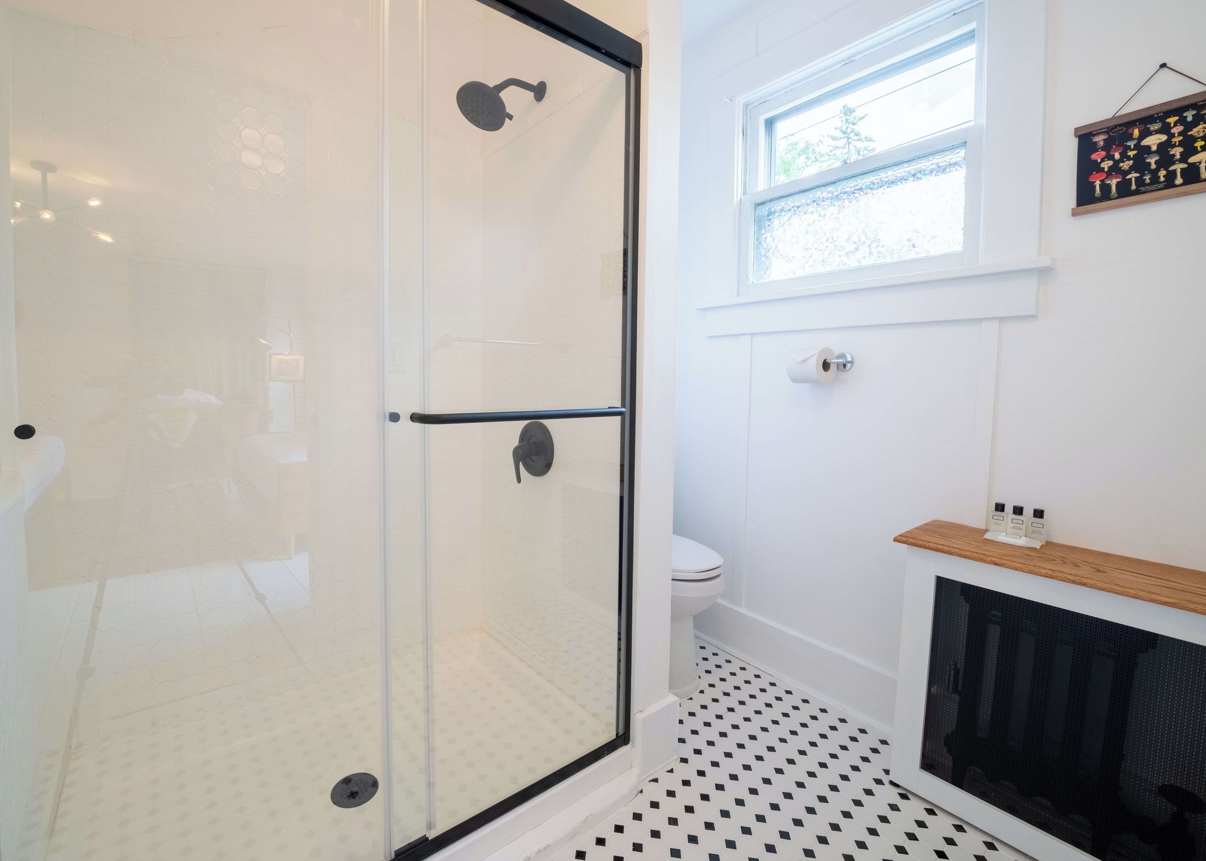 A modern bathroom with a glass shower enclosure, a toilet, and a window providing natural light.