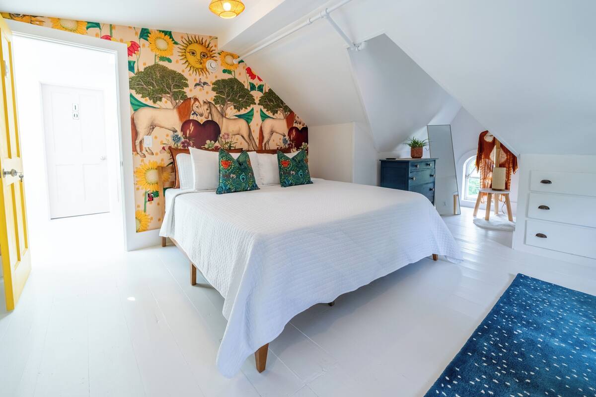 Ein Schlafzimmer mit einem großen Bett, einer Wandmalerei, einer Deckenleuchte und einem Fenster.