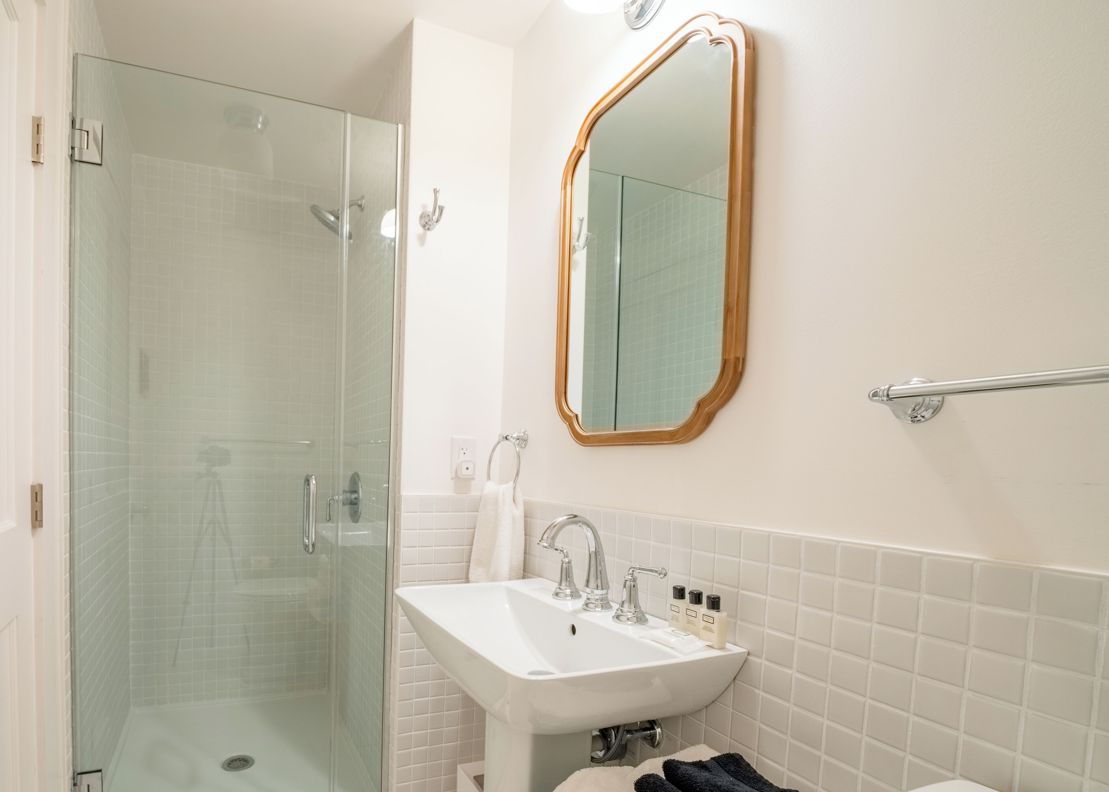 A bathroom with a glass-enclosed shower, a white sink with two faucets, and a mirror with a wooden frame.