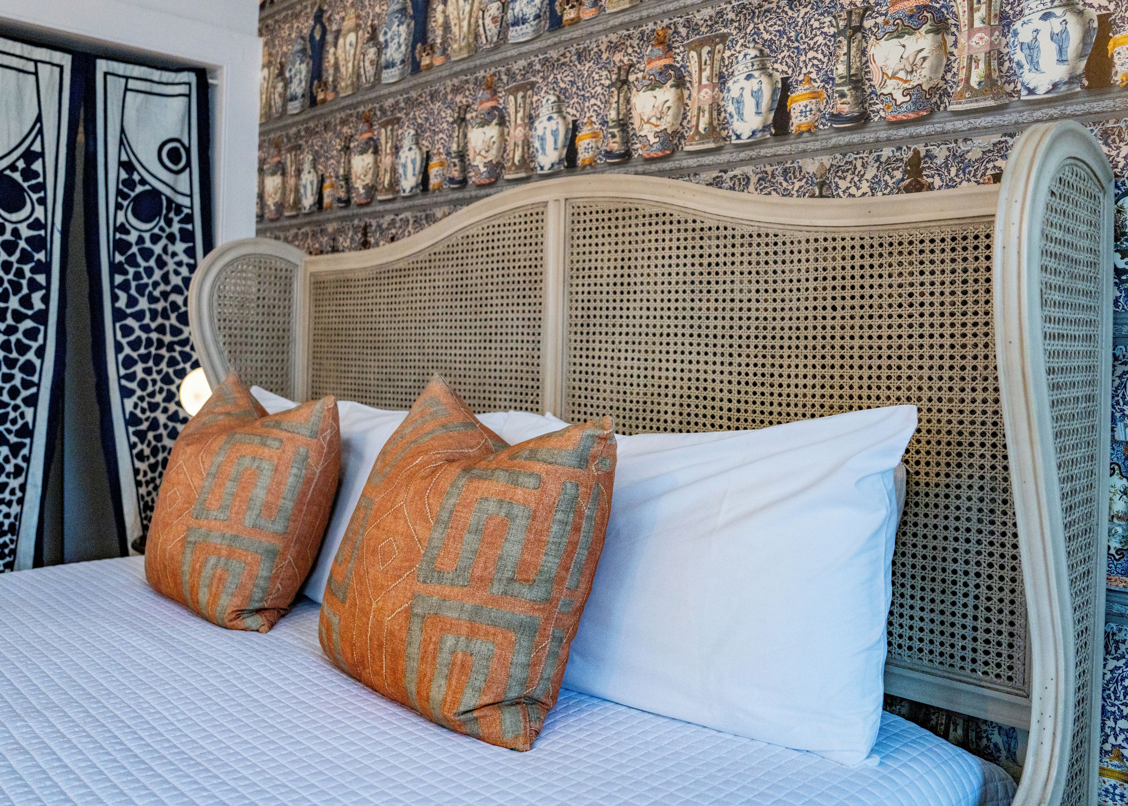 A bed with patterned pillows, a woven headboard, and a wall decorated with ceramic vases.