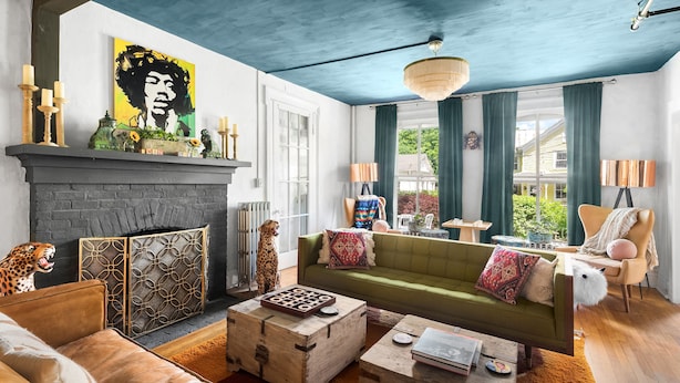 Een woonkamer met een open haard, een groene bank en een fauteuil met luipaardprint.