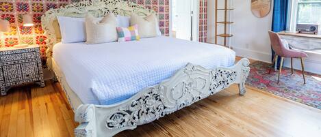 Une chambre avec un grand lit, un plancher en bois, un mur à motifs, un bureau avec une chaise et une échelle.