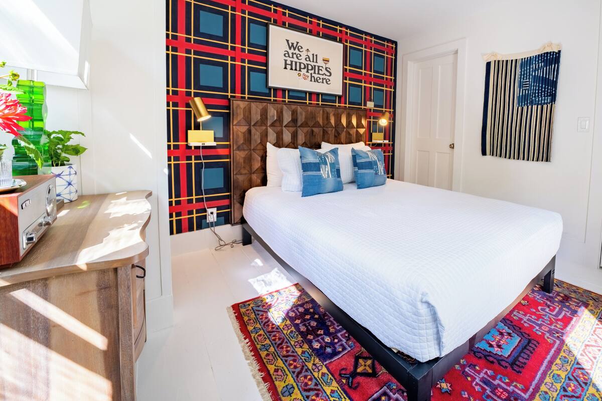 Ein modernes Schlafzimmer mit einer Wand im geometrischen Muster, einem Bett mit weißer Bettwäsche und einem farbenfrohen Teppich.