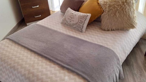A neatly made bed with a patterned bedspread, a wooden nightstand with drawers, and a fluffy pillow. - Hostal Casa Lantana Usaquén - Hostel (Bogotá)