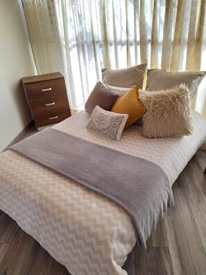 A neatly made bed with a patterned bedspread, a wooden nightstand with drawers, and a fluffy pillow. - Hostal Casa Lantana Usaquén - Hostel (Bogotá)