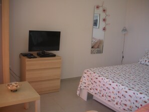 Un dormitorio con cama, cómoda, televisor encima y espejo en la pared.