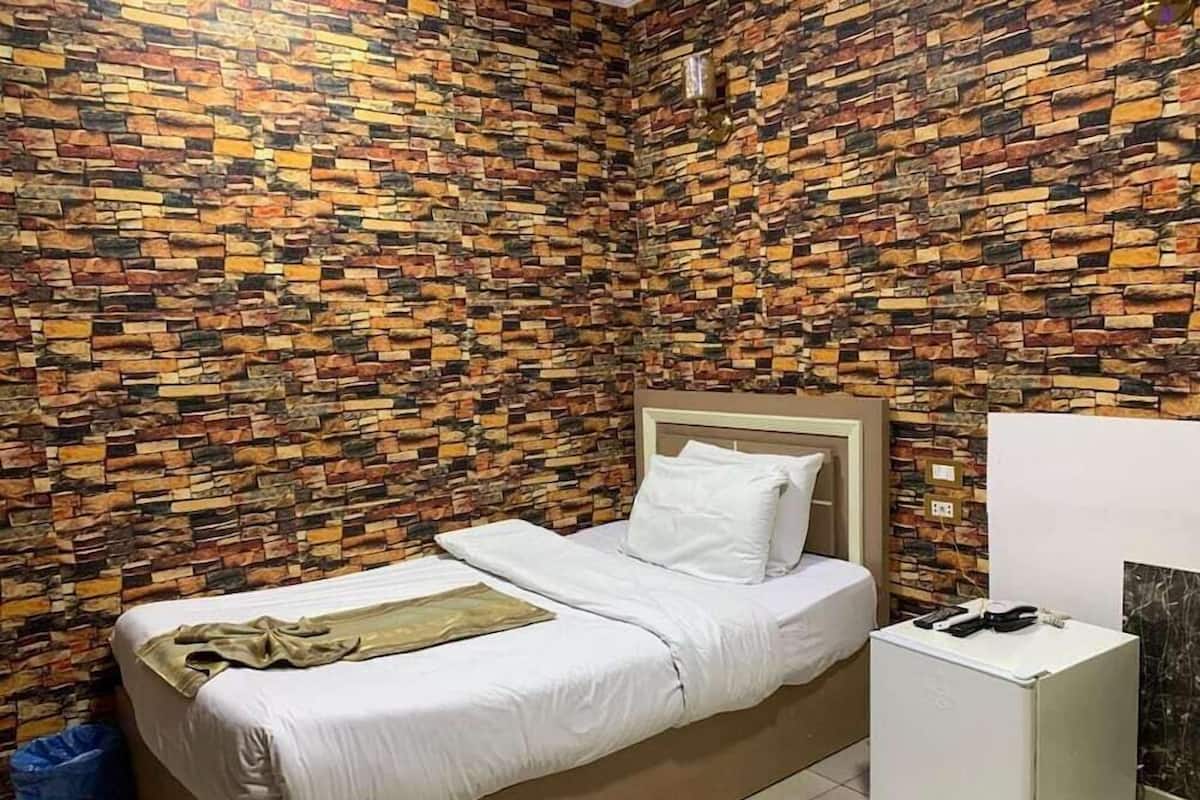A room with a bed, a small white nightstand, and a wall covered in a patterned brick-like design.
