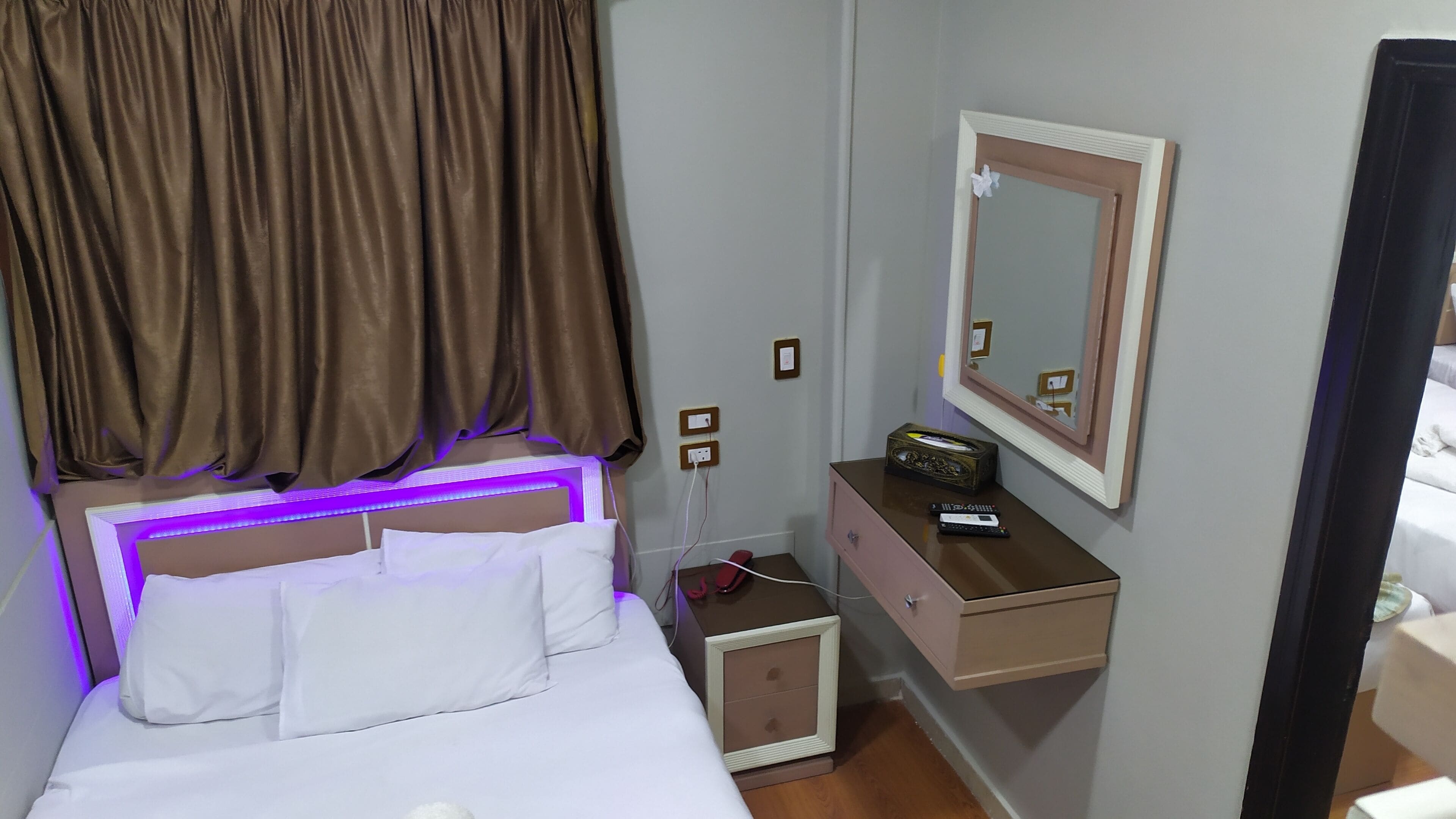 Una habitación de hotel con una cama, una mesita de noche, un aparador, un espejo y una lámpara fijada a la pared.