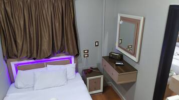 Una habitación de hotel con una cama, una mesita de noche, un aparador, un espejo y una lámpara fijada a la pared.