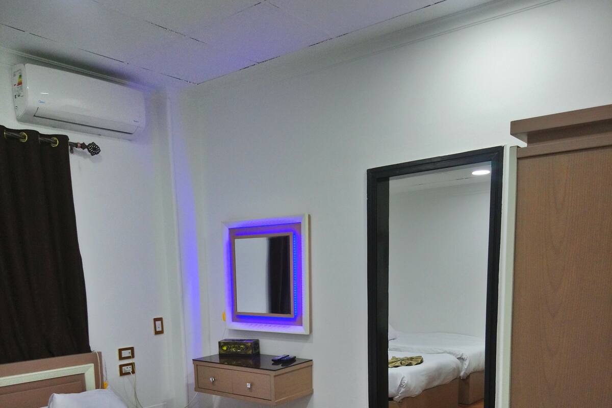 A hotel room with a bed, bedside table, mirror, and an air conditioning unit.