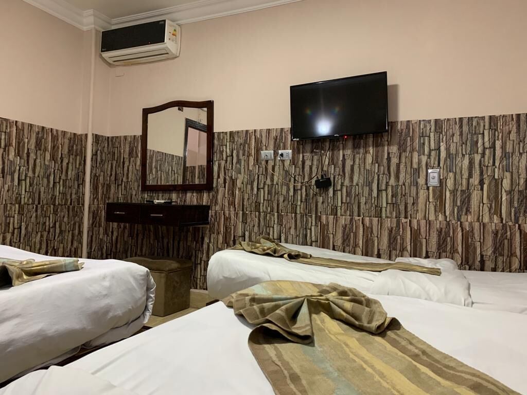 A hotel room with two beds, a flat-screen TV mounted on the wall, a mirror, and a wooden-patterned wall.