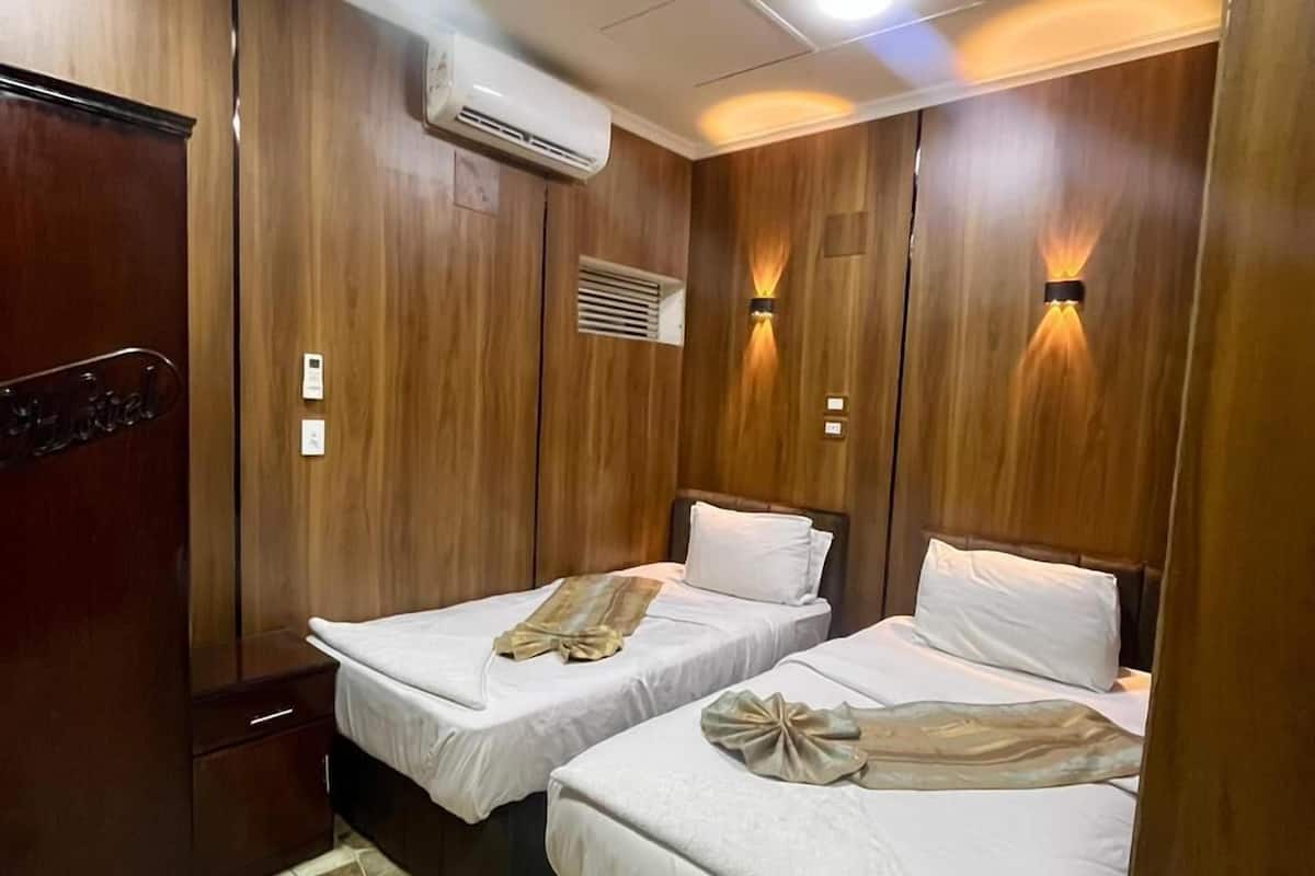 A hotel room with two beds, wooden paneling, an air conditioning unit, and a tiled floor.