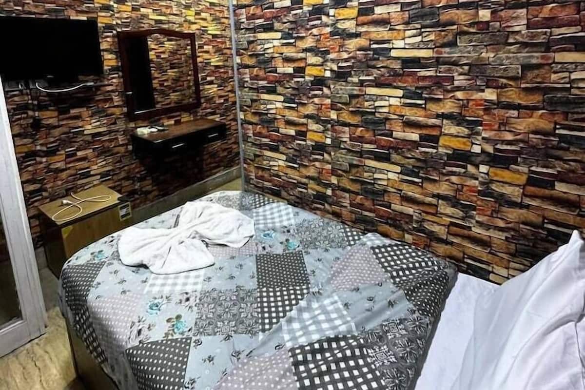 A room with a bed, a flat-screen TV mounted on the wall, and a wooden dresser.