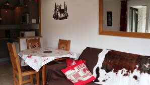 A cozy living room with a brown sofa, a dining table with chairs, and a kitchen in the background. - Lovely 2-room apartment, slopeside, sleeps 6 (Les Orres)