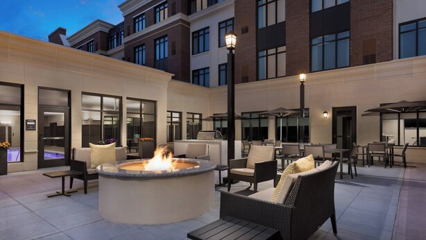 A rooftop patio with a fire pit, outdoor seating, and a view of the building's brick facade.