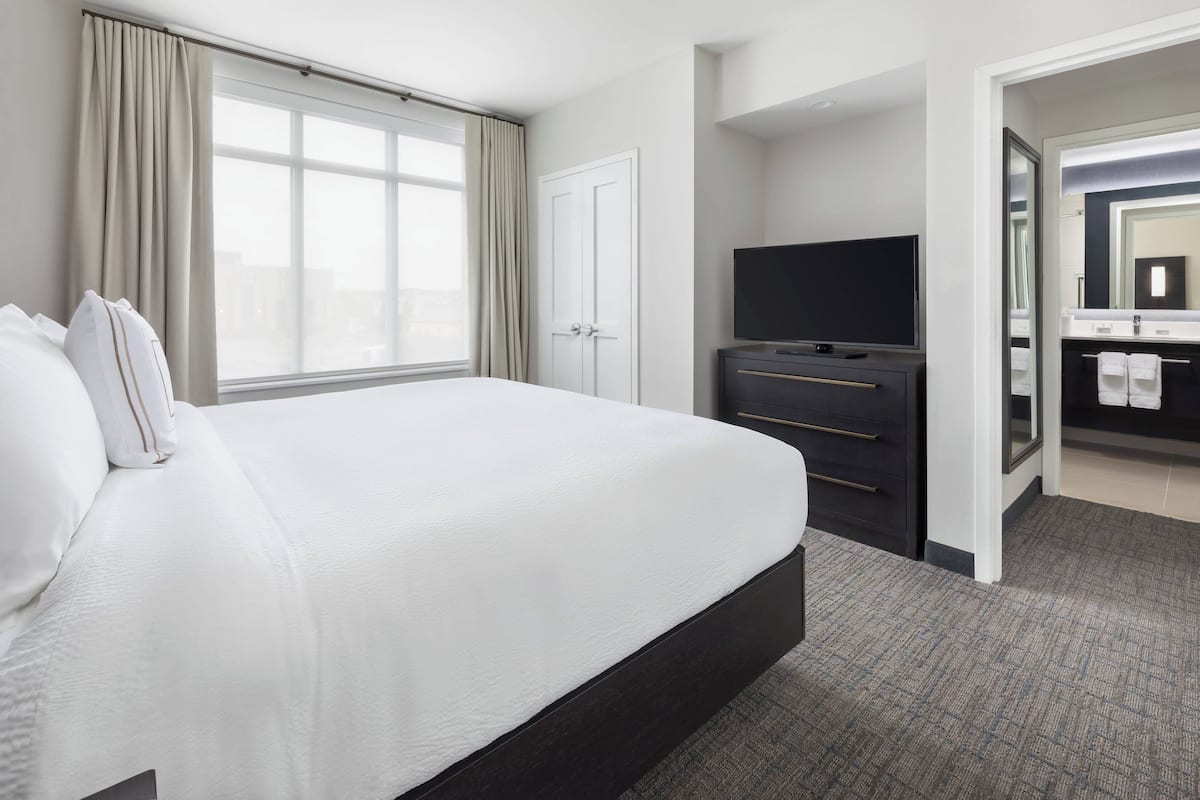 Ein Hotelzimmer mit einem großen Bett, einem Fernseher, einer dunklen Kommode und einem durch eine offene Tür einsehbaren Badezimmer.