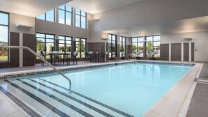 A swimming pool with clear blue water, surrounded by a tiled deck and a seating area with chairs and tables.