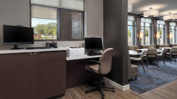 Un espacio de oficina moderno con dos puestos de trabajo equipados con computadoras, una impresora y una zona de estar cómoda con mesas y sillas.