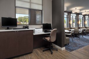 Un espacio de oficina moderno con dos puestos de trabajo equipados con computadoras, una impresora y una zona de estar cómoda con mesas y sillas.