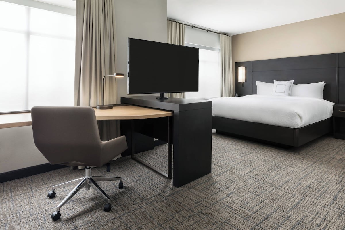 Ein Hotelzimmer mit Bett, Schreibtisch, Flachbildfernseher, Stuhl und Lampe.