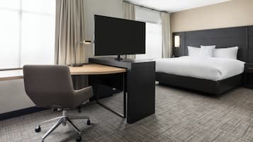 A hotel room with a bed, a desk with a flat-screen TV, a chair, and a lamp.
