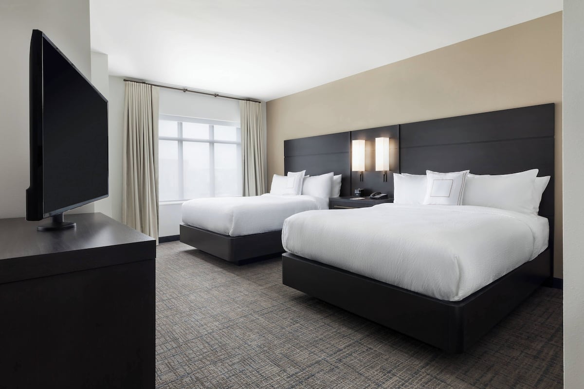Ein Hotelzimmer mit zwei Betten, einem Fernseher und einem großen Fenster mit Vorhängen.
