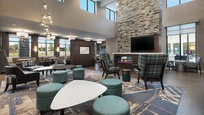 A spacious lobby with high ceilings, large windows, a fireplace, comfortable seating, and a flat-screen TV.