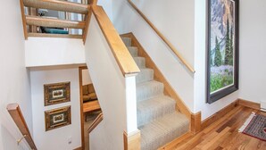A staircase with wooden steps and a carpeted landing, leading to a room with a large window and a framed picture on the wall. - Haymeadow Townhome A1 | 5BR Ski-Out, Private Hot Tub (Avon)