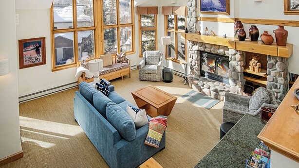 A spacious living room with a large window, a stone fireplace, and a cozy seating area. - Haymeadow Townhome A1 | 5BR Ski-Out, Private Hot Tub (Avon)
