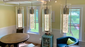 Una habitación con una mesa de comedor, una silla azul y tres lámparas colgantes con efecto brillante.