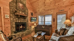 A cozy log cabin interior with a stone fireplace, wooden furniture, and a couch with animal-themed cushions.