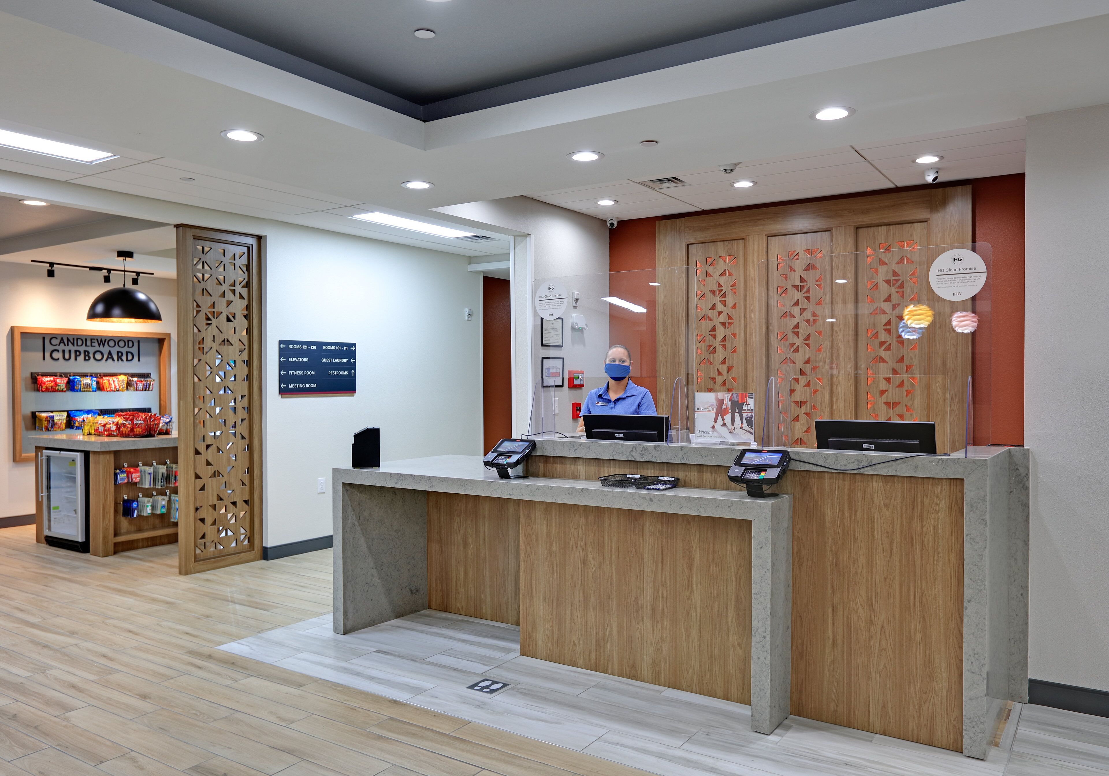 A reception desk with a wooden finish, a computer, and a phone. There is a sign for a candlewood cupboard and a directory on the wall.
