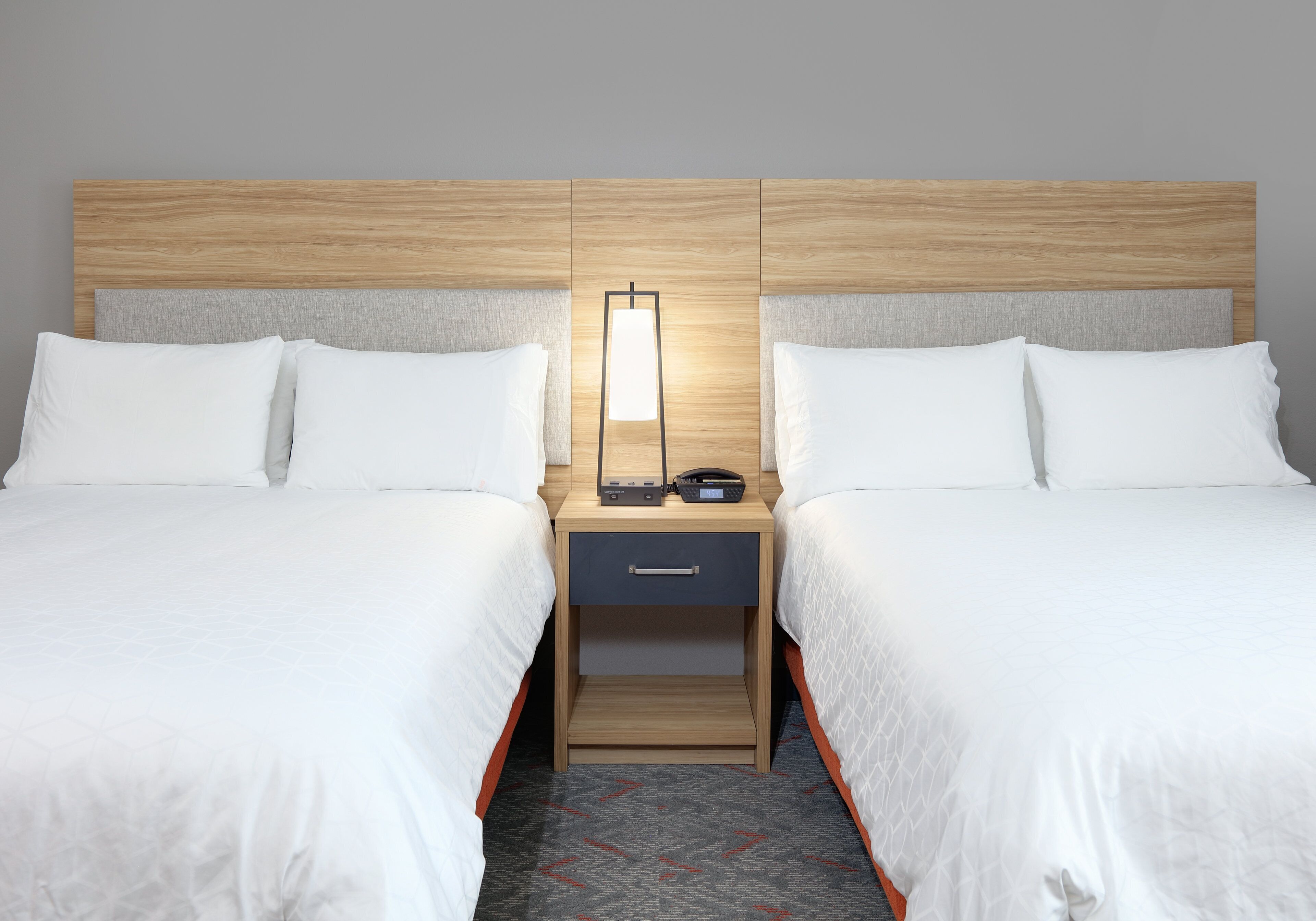 A hotel room with two beds, a nightstand between them, and a bedside table with a lamp.