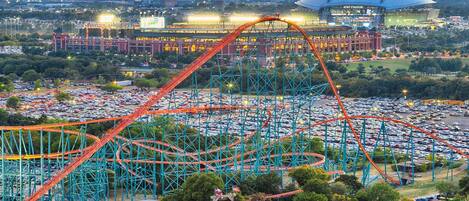 Des montagnes russes dans un parc d’attractions, avec un stade en arrière-plan.