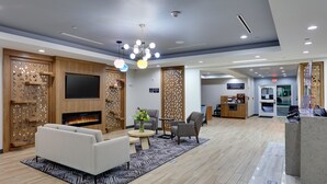Un hall d’hôtel moderne doté d’une cheminée, d’un espace salon et d’un coin café.