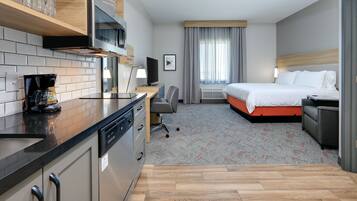 Una habitación de hotel con kitchenette, cama, escritorio y televisor.