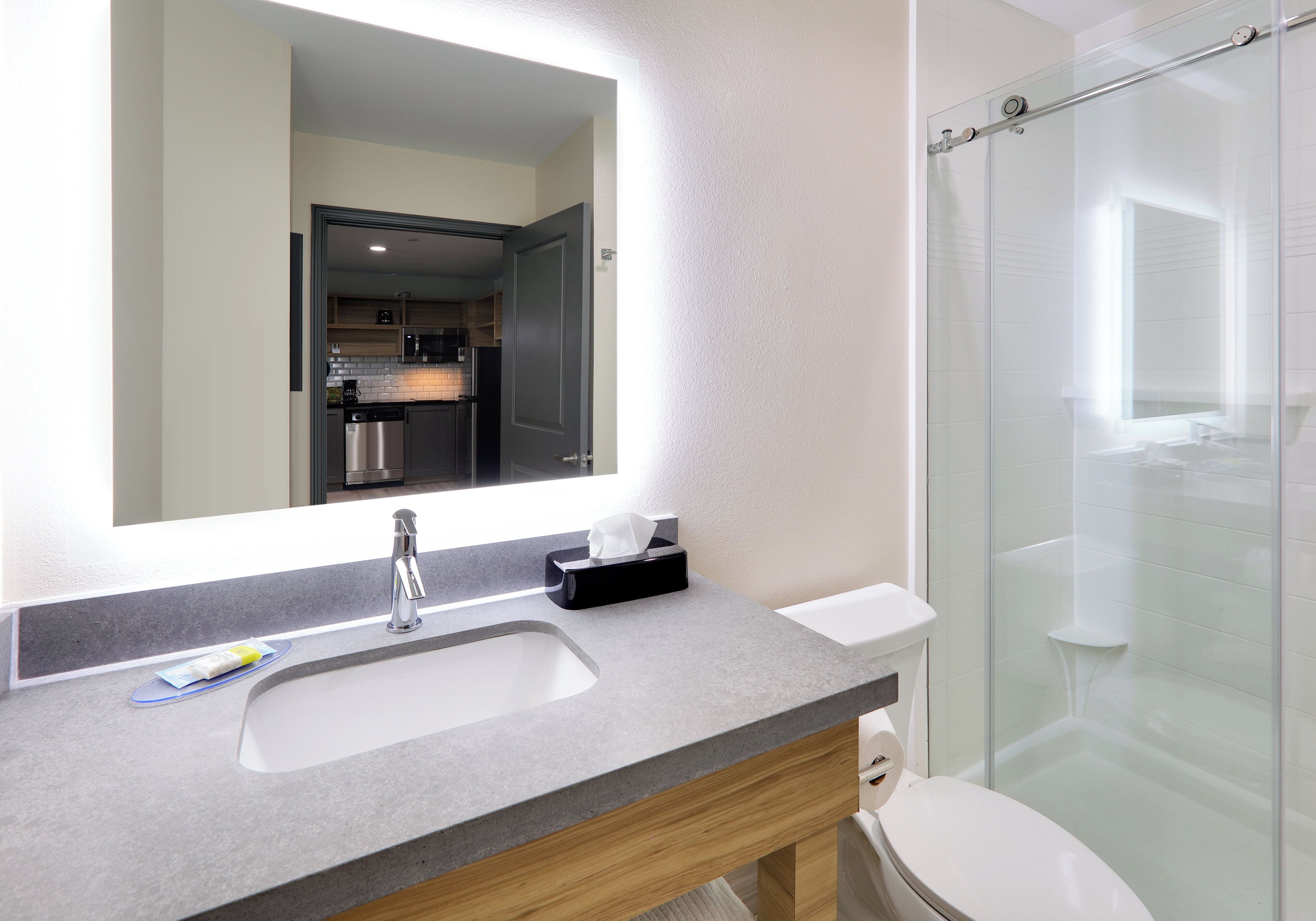 Un baño moderno con un espejo grande, un lavamanos, un inodoro y una cabina de ducha de vidrio.