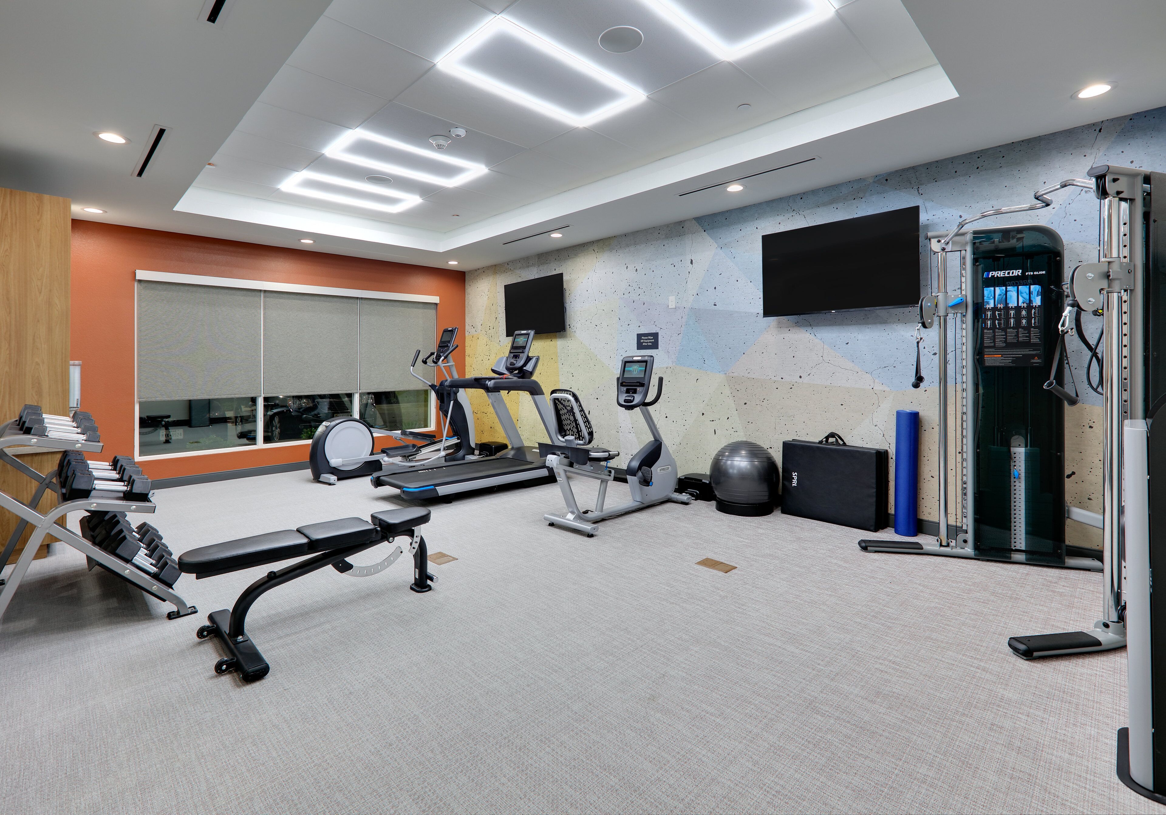 A modern gym with cardio machines, weightlifting equipment, and a large mirror.