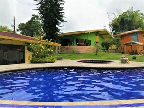 A swimming pool with a clear blue water surface, surrounded by a grassy area and a building with a green roof. - Ecohotel La Casona (Pereira)
