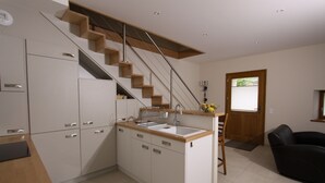 A modern kitchen with a wooden staircase, white cabinets, and a small island with a sink.