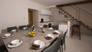 Et moderne spiseområde med et langt bord dækket til seks personer, et køkken i baggrunden og en trappe til en etage over.