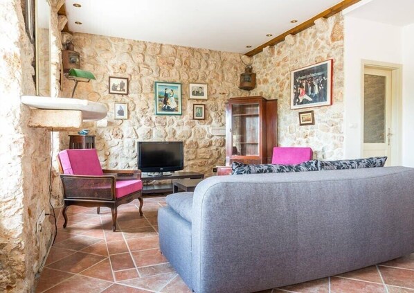 Una sala de estar acogedora con paredes de piedra, un televisor de pantalla plana, un sofá y un mueble con fotografías.